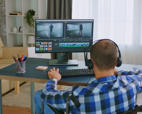 Using post production software Invalid man in wheelchair editing a video using post production software wearing headphones.